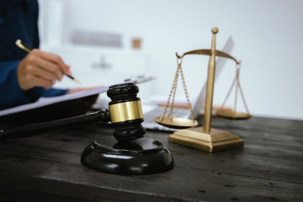 Gavel, scales of justice, and a lawyer's hand writing.
