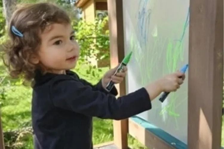Young girl drawing on an easel with markers.