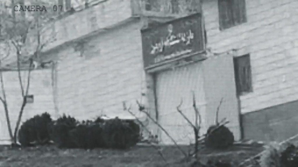 Grayscale security camera footage of an explosion at Evin Prison's gate.