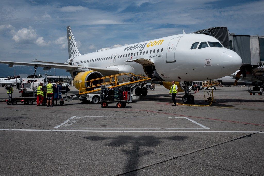 Baggage handlers loading luggage onto a Vueling Airbus A320 airplane.