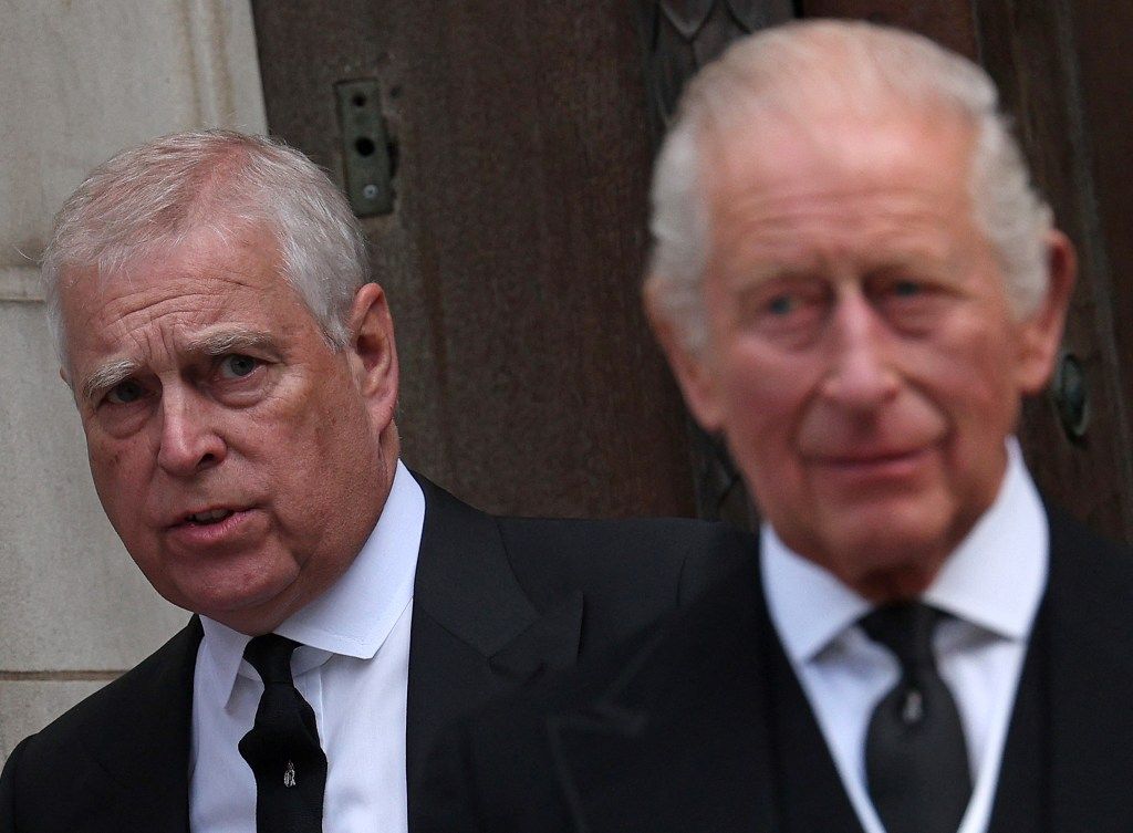 Prince Andrew with King Charles III blurred in the background.