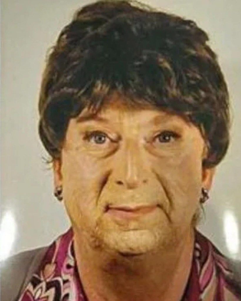A person in a wig and makeup, with visible stubble on their face.