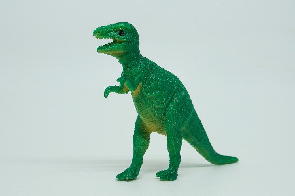 Green plastic Tyrannosaurus Rex toy with an open mouth, standing on a white background.