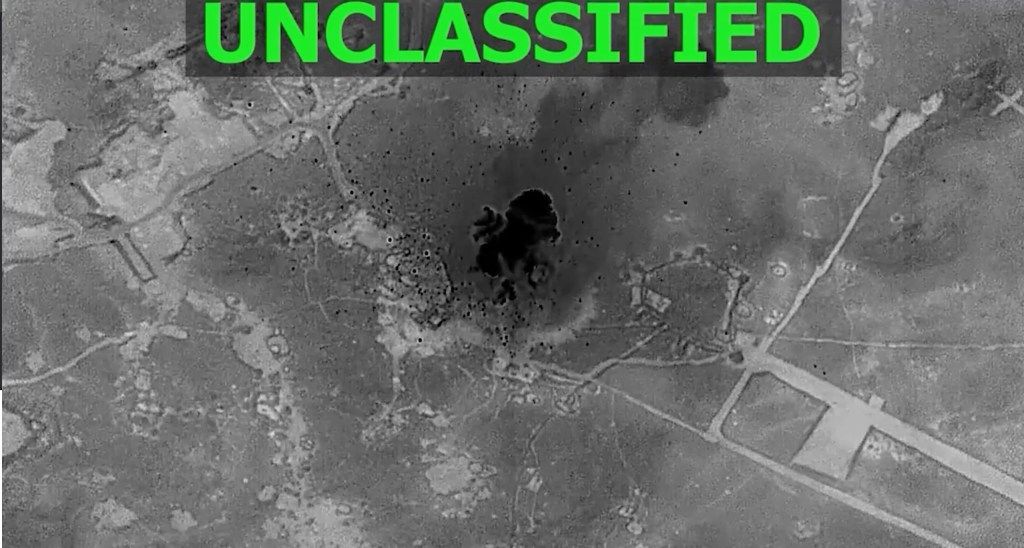 Black and white aerial image shows an explosion with a large black cloud and smoke in the center of a military target area.