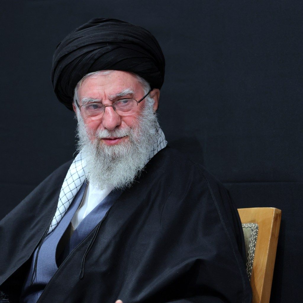 Ayatollah Ali Khamenei, in a black turban and robe, attends a mourning ceremony.