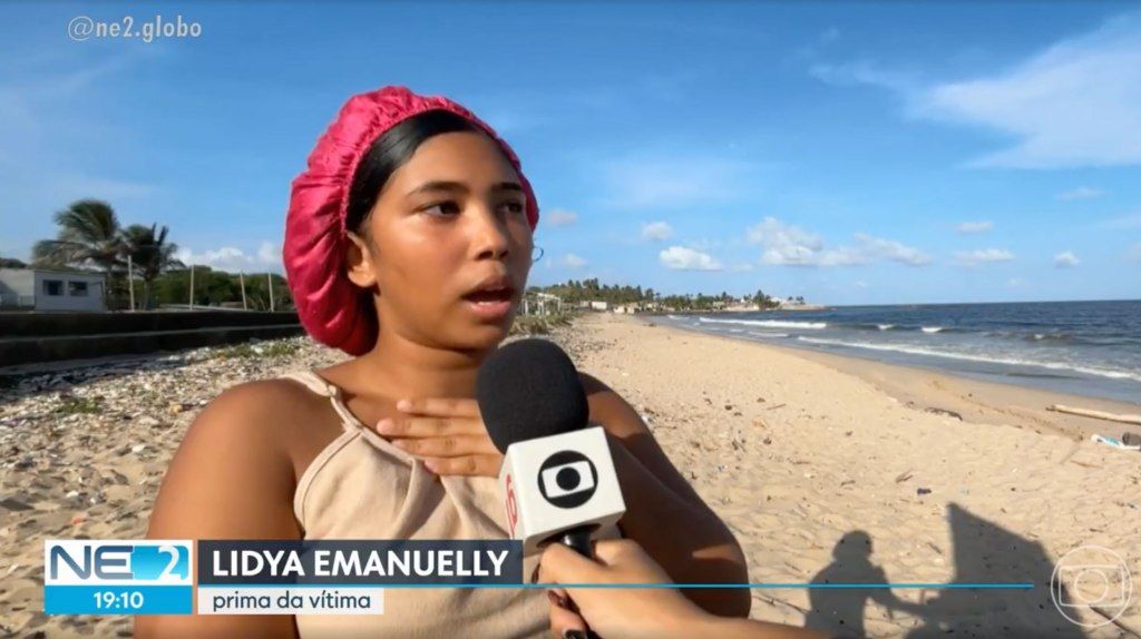 Lídia Emanuelle, cousin of shark attack victim Deivson Rocha Dantas, interviewed on a sandy beach.