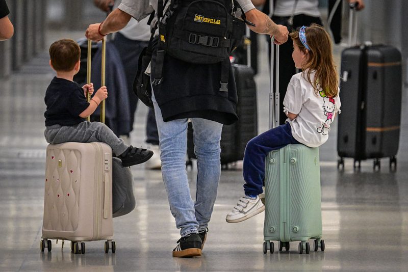 A person rolls two suitcases with children seated on them as travelers pass through Miami International Airport during Memorial Day weekend on May 24, 2025 in Miami, Florida. This Memorial Day, travel is expected to break records according to AAA, with an estimated 45.1 million travelers. About 3.6 million of those expected travelers will be flying to their destinations. (Photo by Giorgio VIera / AFP) (Photo by GIORGIO VIERA/AFP via Getty Images)