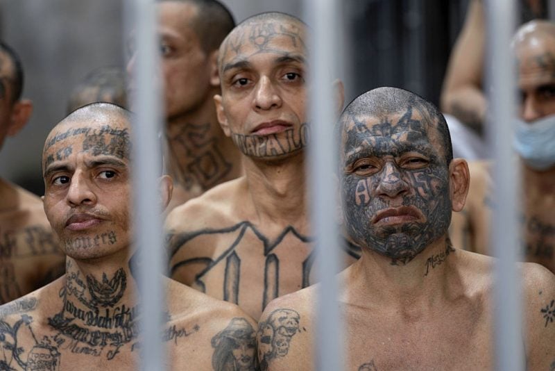TECOLUCA, EL SALVADOR - DECEMBER 15: Inmates look from their cell at CECOT (Counter Terrorism Confinement Center) on December 15, 2025 in Tecoluca, El Salvador. Officials had instructed them to remove their shirts to display gang-affiliated tattoos. CECOT gained notoriety in 2025 when the Trump administration began its controversial policy of deporting people to El Salvador who they claimed were members of the Venezuelan criminal organization Tren De Aragua, and Mara Salvatrucha (MS-13), a gang whose members are historically Salvadoran. In 2023 El Salvador opened Latin America's largest prison as part of President Nayib Bukele's plan to fight gangs. The government says some 20,000 gang members are being held at the mega-prison, which has a capacity of 40,000. (Photo by John Moore/Getty Images)