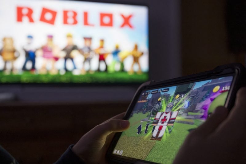 This illustration photograph shows a child posing as he plays a video game on a tablet on the online game platform and game creation system Roblox developed by Roblox Corporation in Terville, northeastern France on March 11, 2026. (Photo by Jean-Christophe VERHAEGEN / AFP via Getty Images)