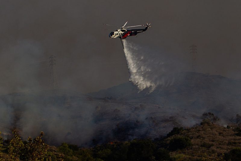 CORRECTION / A Fire Department helicopter drops water on the Sandy Fire as it burns in the hills near a residential area in Simi Valley, California on May 18, 2026. A brush fire broke out May 18 in the suburbs of Los Angeles, spreading rapidly and prompting authorities to issue evacuation orders for thousands of residents. Dubbed the Sandy Fire, the blaze broke out late morning in Simi Valley, a city of roughly 125,000 residents about 40 miles (60 kilometers) northwest of downtown Los Angeles. (Photo by Apu GOMES / AFP via Getty Images) / "The erroneous mention[s] appearing in the metadata of this photo by Apu GOMES has been modified in AFP systems in the following manner: [May 18] instead of [May 15]. Please immediately remove the erroneous mention[s] from all your online services and delete it (them) from your servers. If you have been authorized by AFP to distribute it (them) to third parties, please ensure that the same actions are carried out by them. Failure to promptly comply with these instructions will entail liability on your part for any continued or post notification usage. Therefore we thank you very much for all your attention and prompt action. We are sorry for the inconvenience this notification may cause and remain at your disposal for any further information you may require."