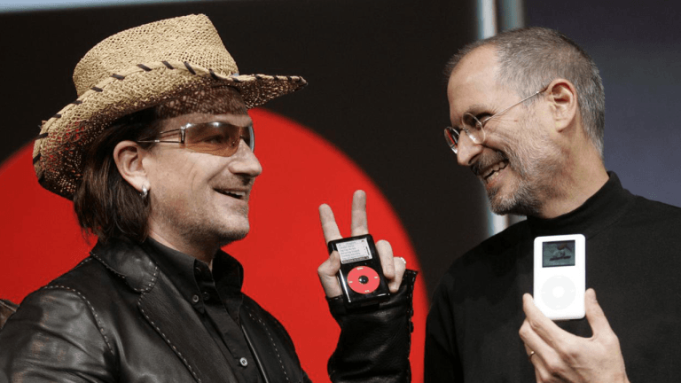 Bono and Steve Jobs smile while holding portable music players during a product launch event. Credit photo : 2004 PETER DASILVA/NYT