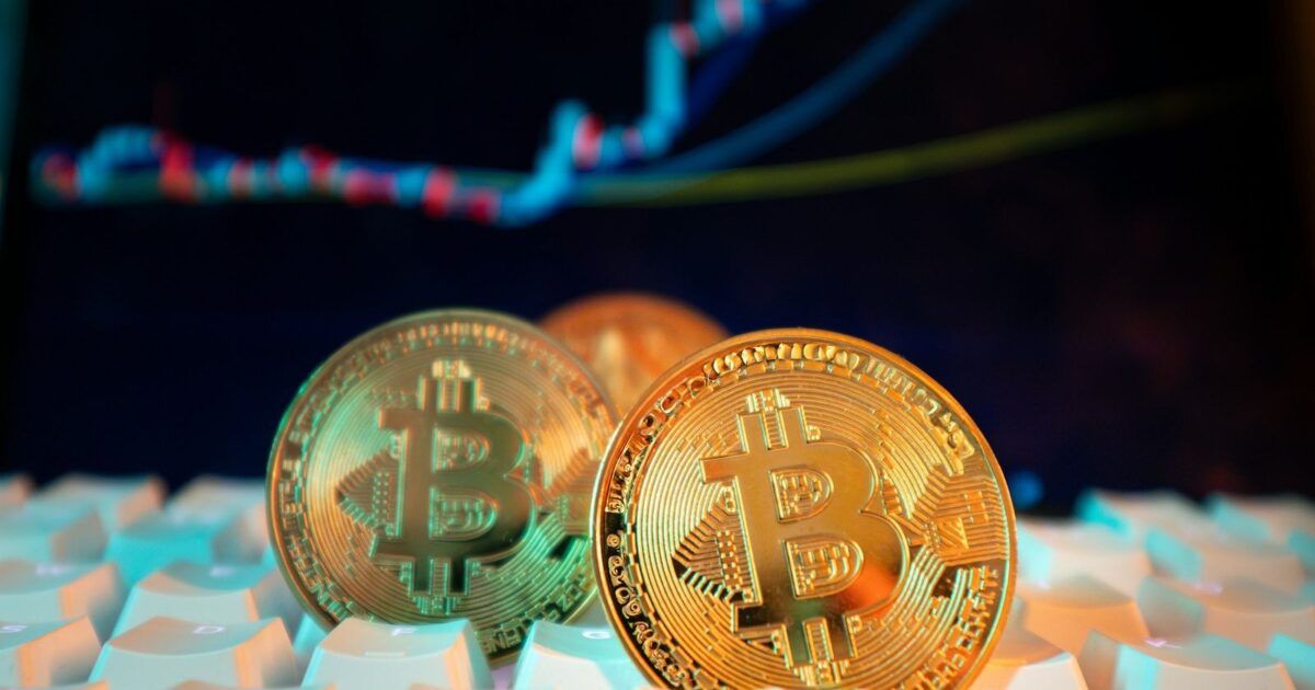 Two physical Bitcoin coins in front of a blurred price display for a story about Fidelity's long-term support model.