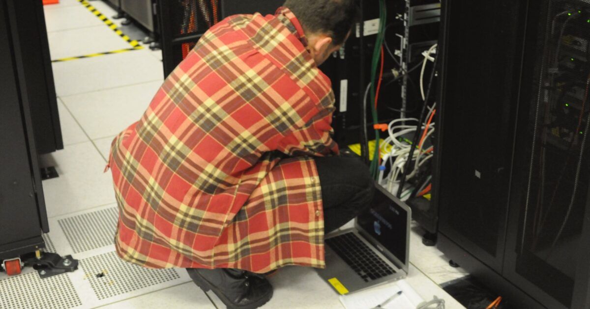 Technician using a laptop beside server racks