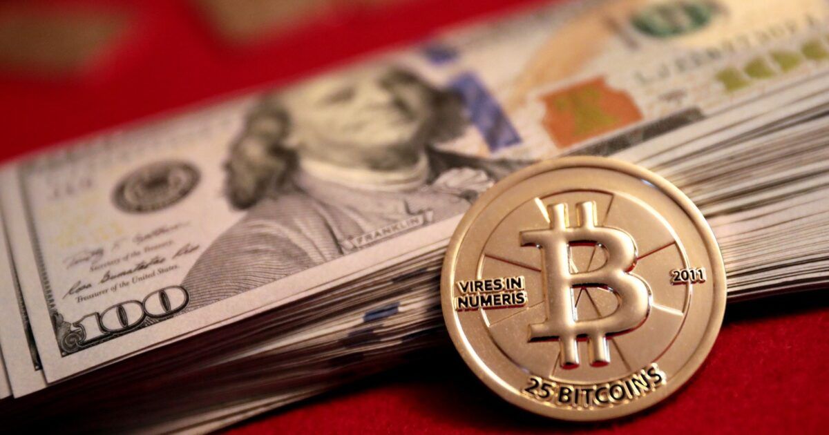 A physical Bitcoin token beside U.S. currency as market-cycle indicators turn positive