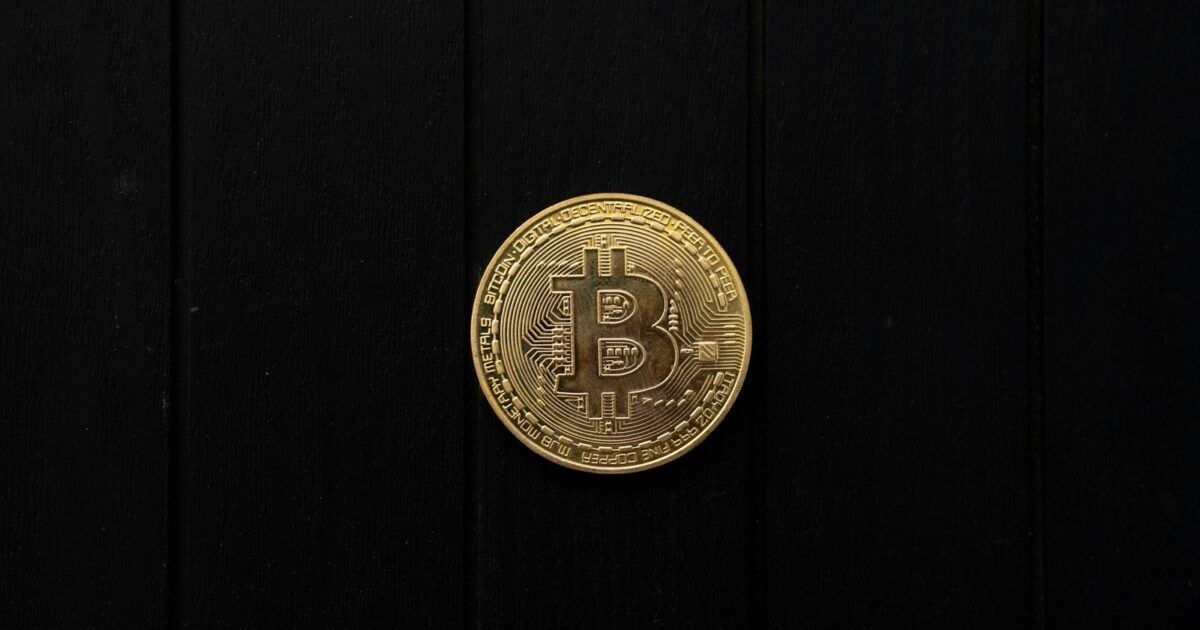 A physical Bitcoin coin isolated against a black wooden background