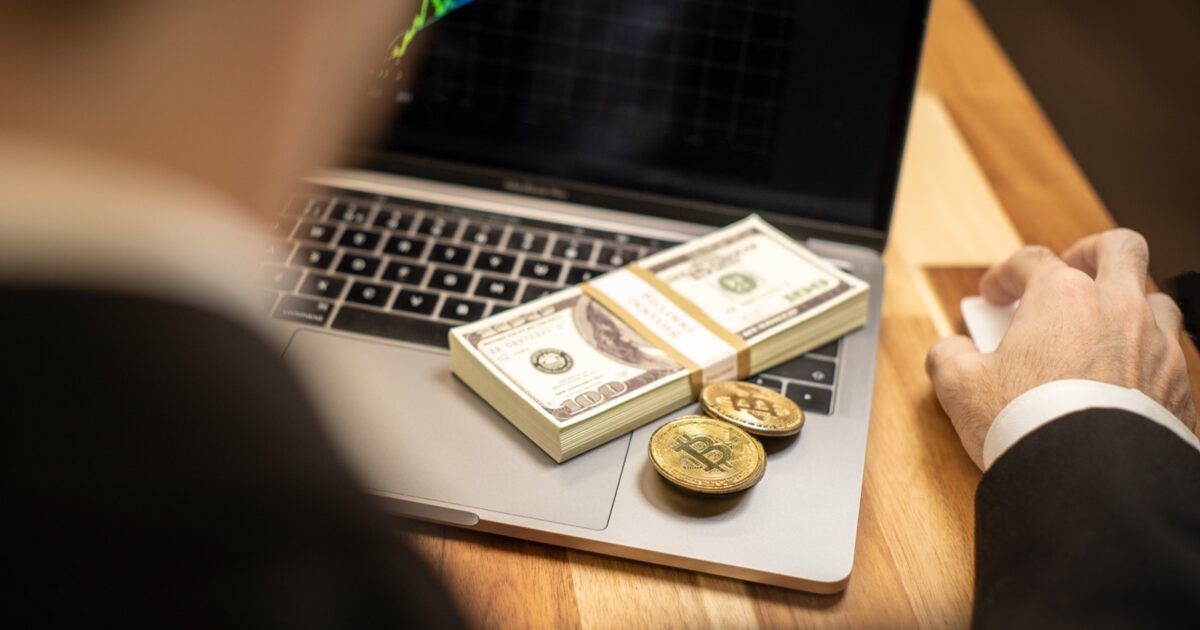 An investor at a laptop with physical Bitcoin coins and cash while weighing portfolio risk