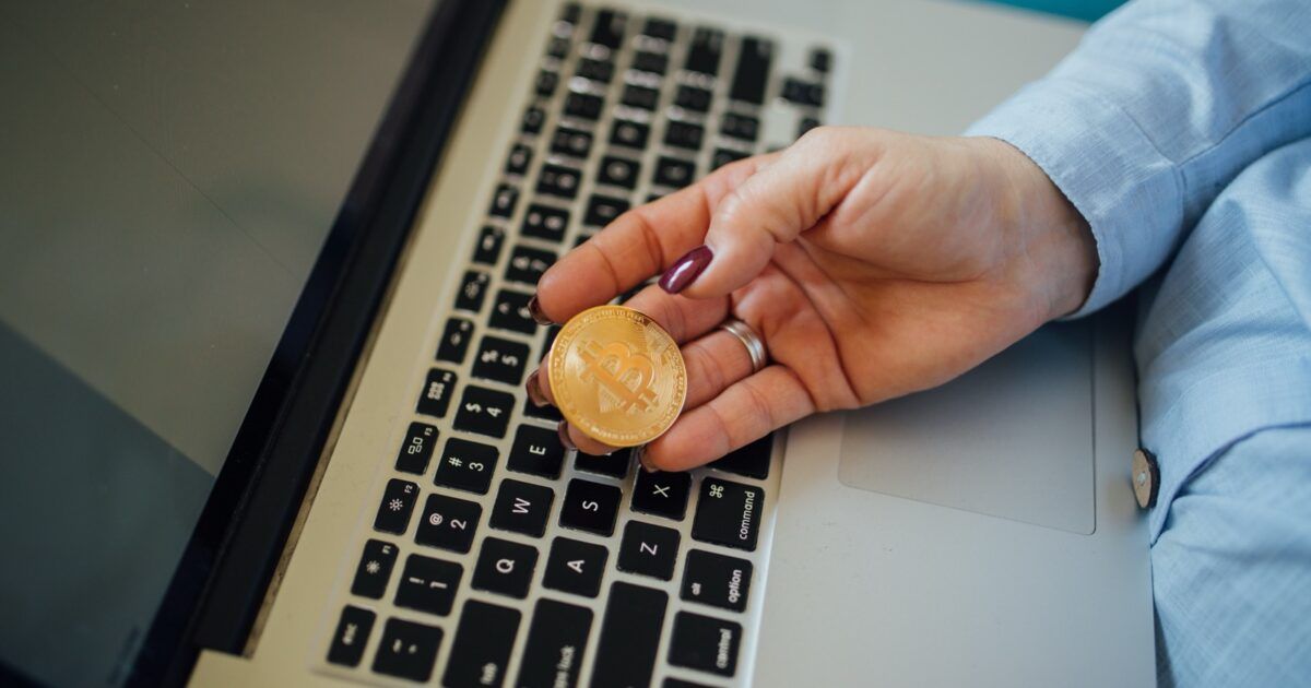 A woman holding a physical Bitcoin token above a laptop keyboard