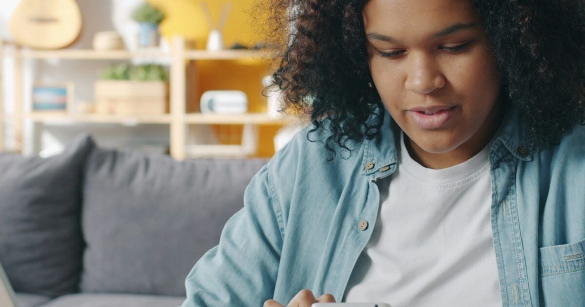 Young adult reviewing a smartphone beside a laptop while managing a long-term investment portfolio