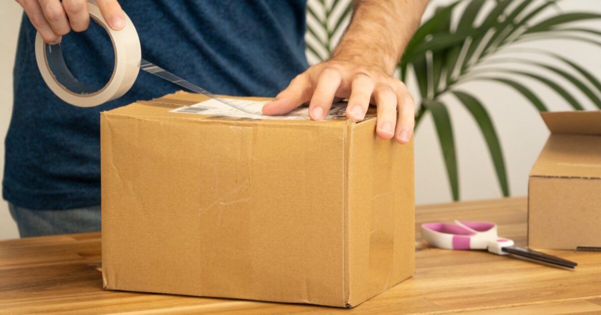 A person sealing a shipping label on a cardboard parcel