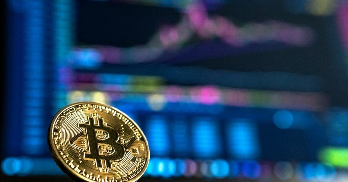 A physical Bitcoin coin in front of a blurred market screen during a fragile weekend rebound