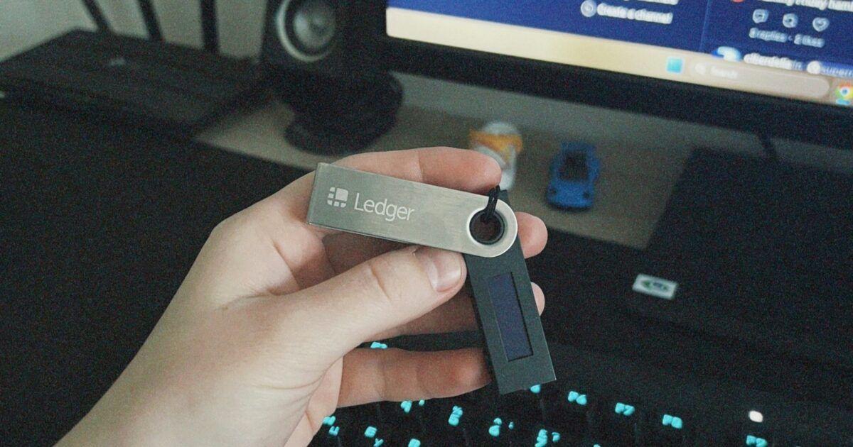 Hand holding a Ledger hardware wallet above a keyboard